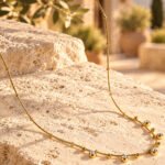 Aurevia Necklace displayed on a stone background with delicate gold sphere and crystal details