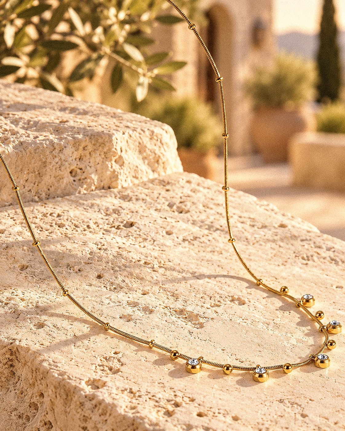 Aurevia Necklace displayed on a stone background with delicate gold sphere and crystal details