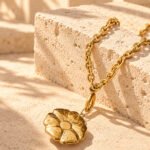 Avelora Necklace placed on a marble background, featuring polished golden rings and engraved silver-toned details