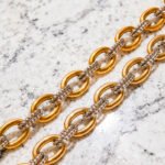 Flat lay of Regia Trama Necklace on marble background with polished gold and silver-toned rings