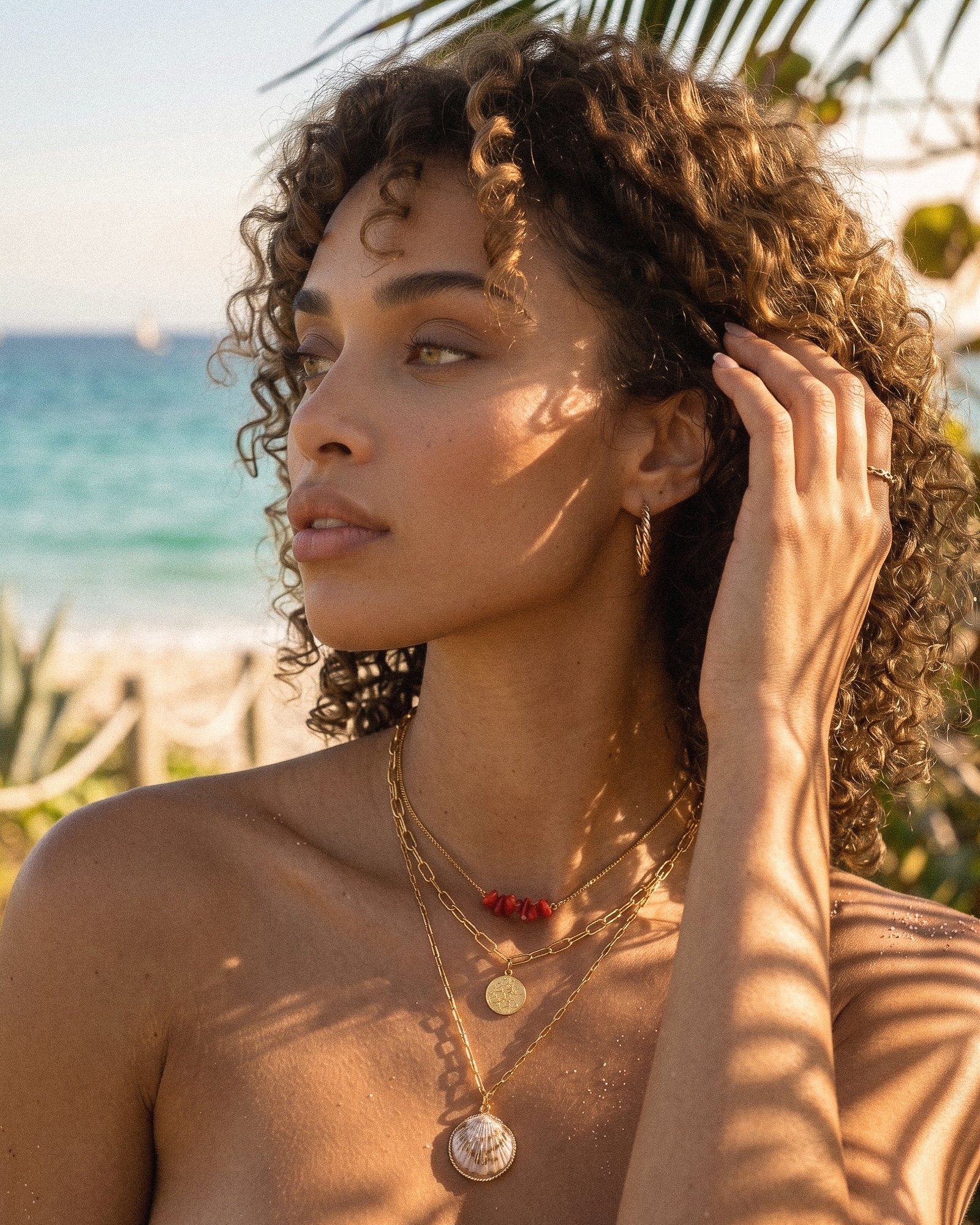 Close-up of Seravelle Necklace on model showing red coral-style beads, gold coin charm, and natural shell pendant