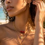 Portrait of a woman wearing Seravelle Necklace with layered gold chains, red beads, and shell pendant