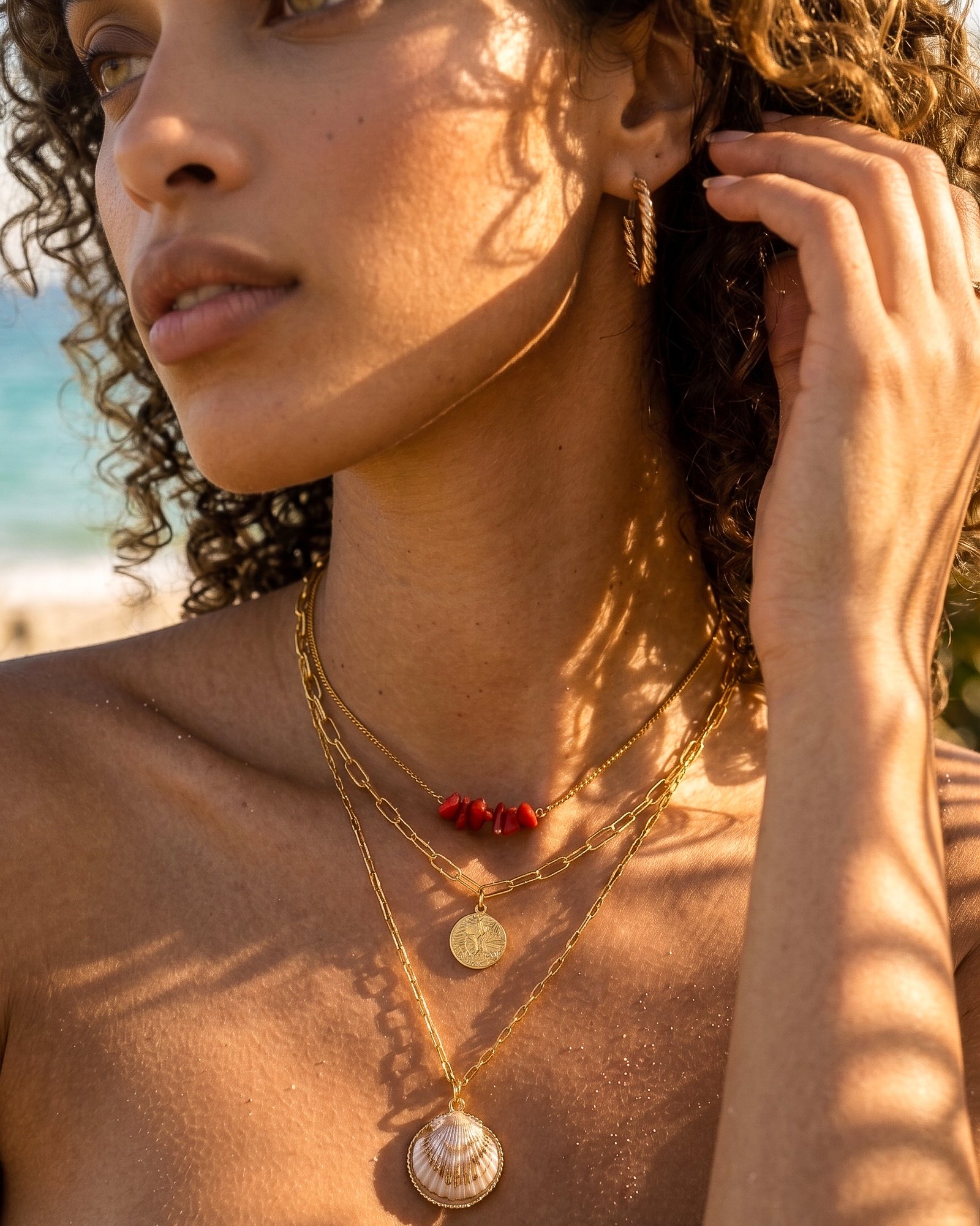 Portrait of a woman wearing Seravelle Necklace with layered gold chains, red beads, and shell pendant