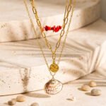 Close-up product image of Seravelle Necklace showing red beads, paperclip links, coin charm, and shell detail