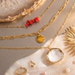 Flat lay of Seravelle Necklace showing three layered chains with red bead, coin, and shell details