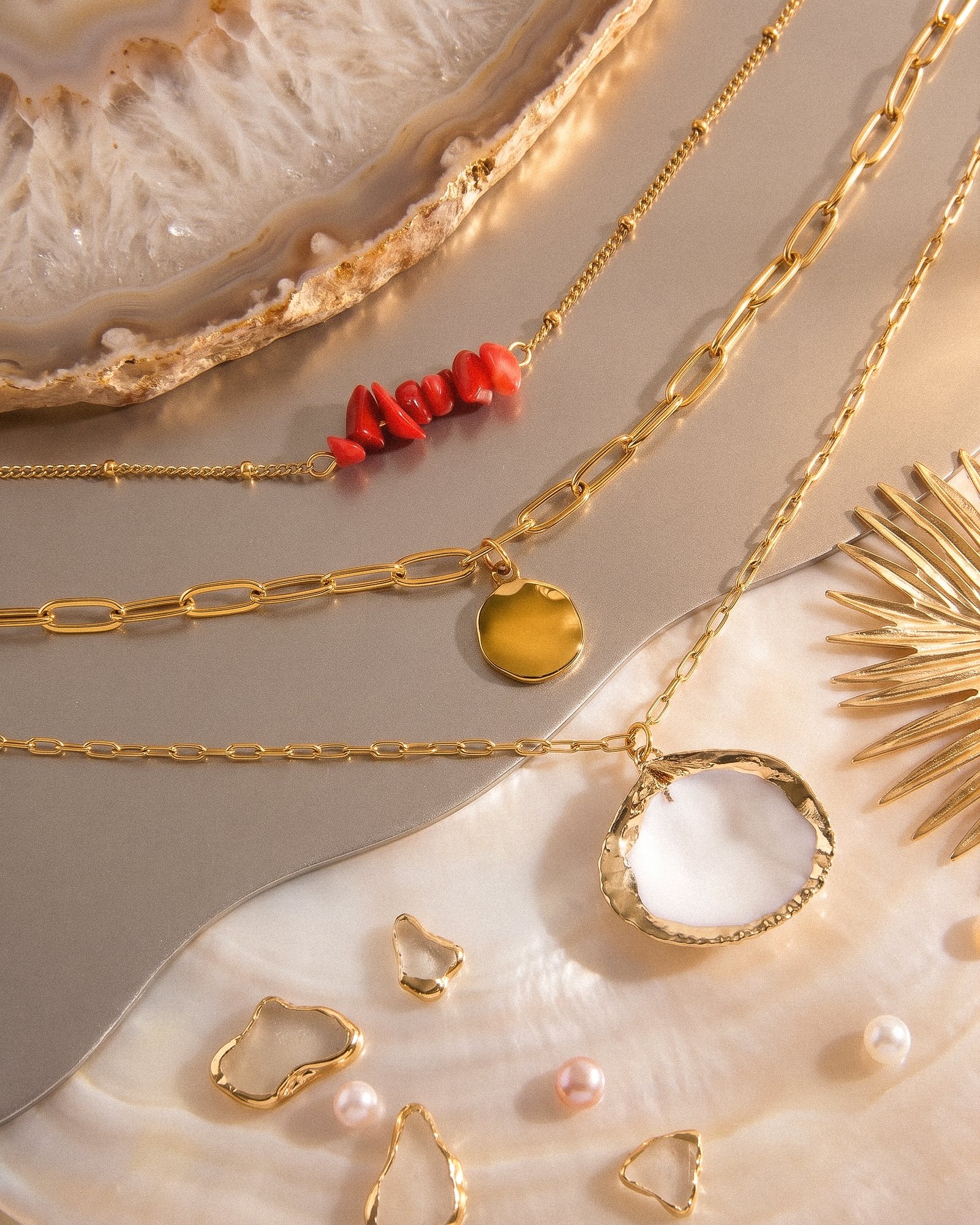Flat lay of Seravelle Necklace showing three layered chains with red bead, coin, and shell details