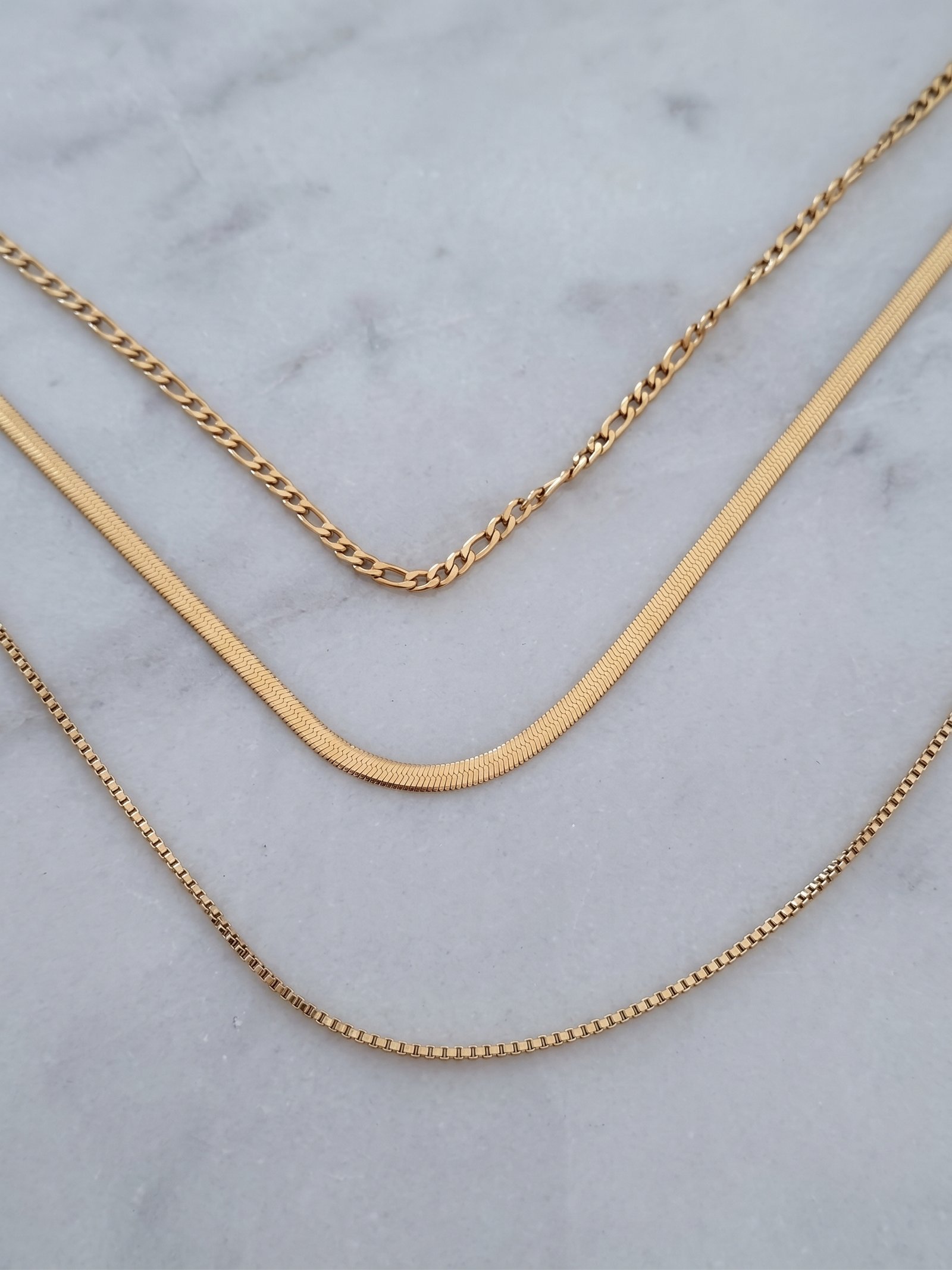 Elvara Necklace on marble background with layered gold chain styling