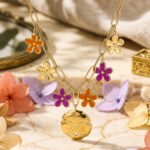 Close-up product image of Fiori Solari Necklace showing colorful flower charms, gold paperclip links, and central medallion detail
