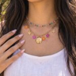 Close-up of Fiori Solari Necklace on a model, showing the gold chain, colorful flower charms, and decorative medallion detail