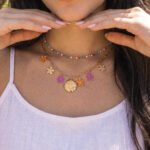 Detailed neckline shot of Fiori Solari Necklace on a model, featuring orange, purple, and gold flower charms