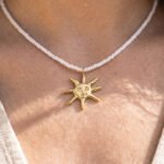 Model wearing Sole Bianco from Mare Amuleti Necklaces, featuring white beads and a gold sun charm