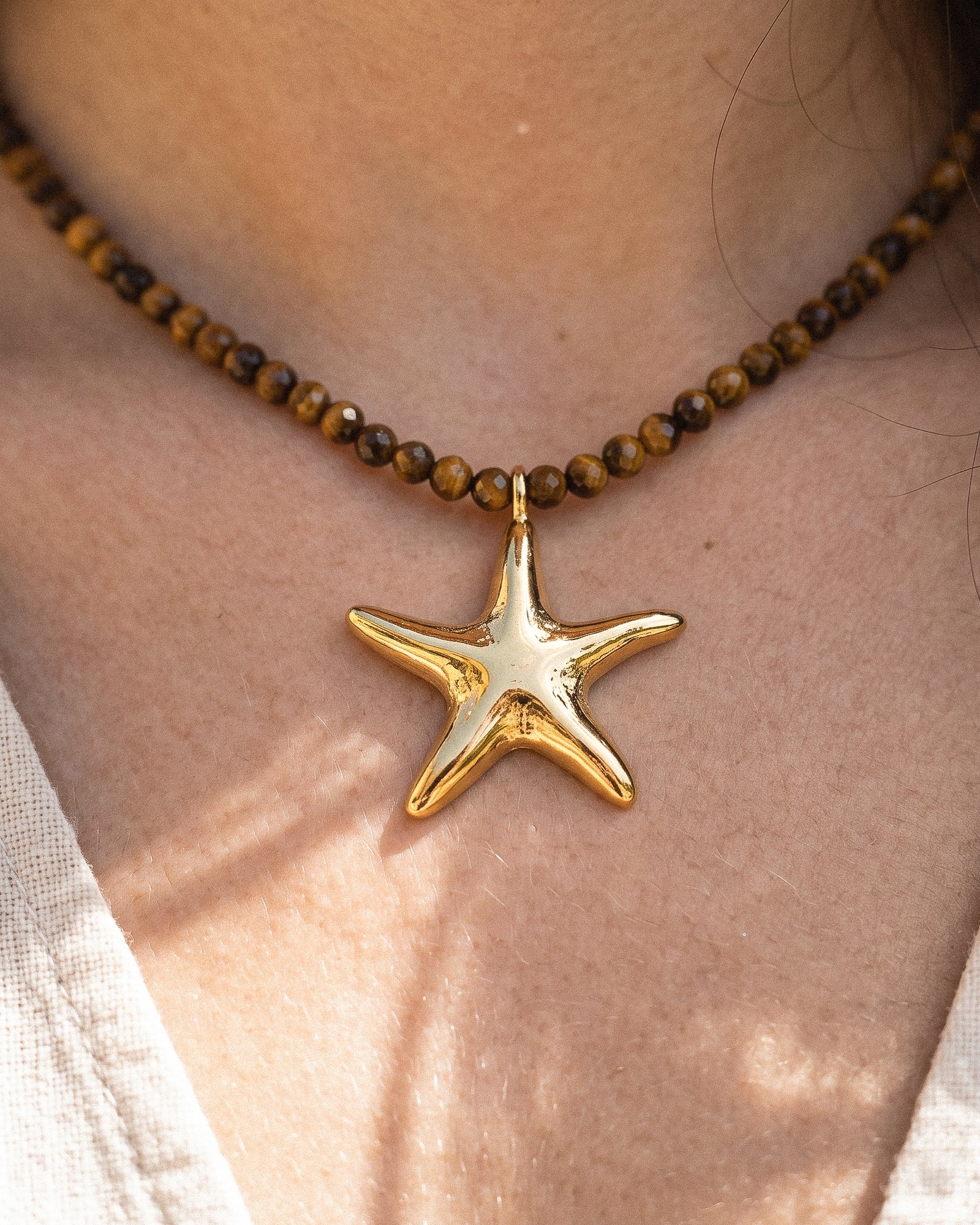 Model wearing Stella Terra from Mare Amuleti Necklaces, featuring brown beads and a gold starfish charm