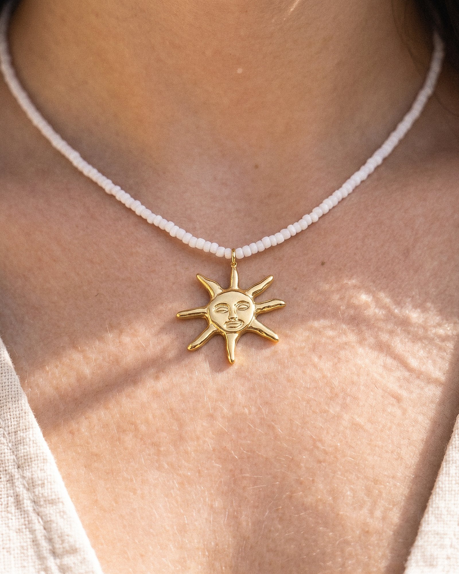 Model wearing Sole Bianco from Mare Amuleti Necklaces, featuring white beads and a gold sun charm