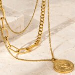 Valessia Necklace flat lay on stone background with layered chains and coin pendant