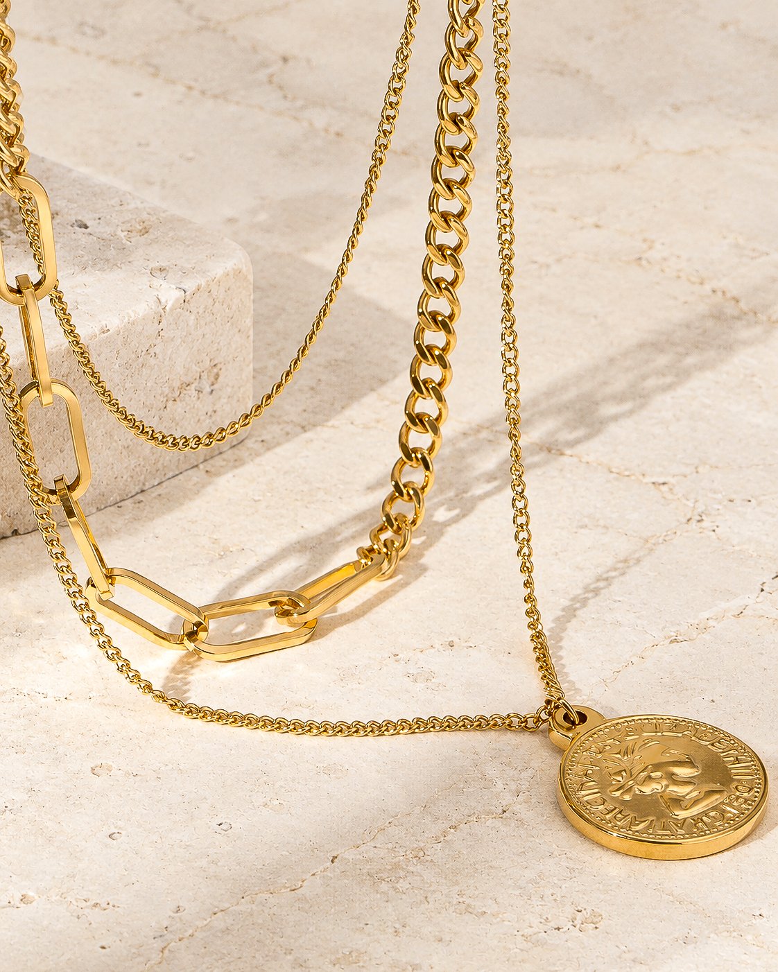 Valessia Necklace flat lay on stone background with layered chains and coin pendant
